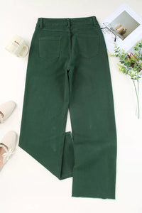 Green pants on a white surface with a floral arrangement and shoes in the background