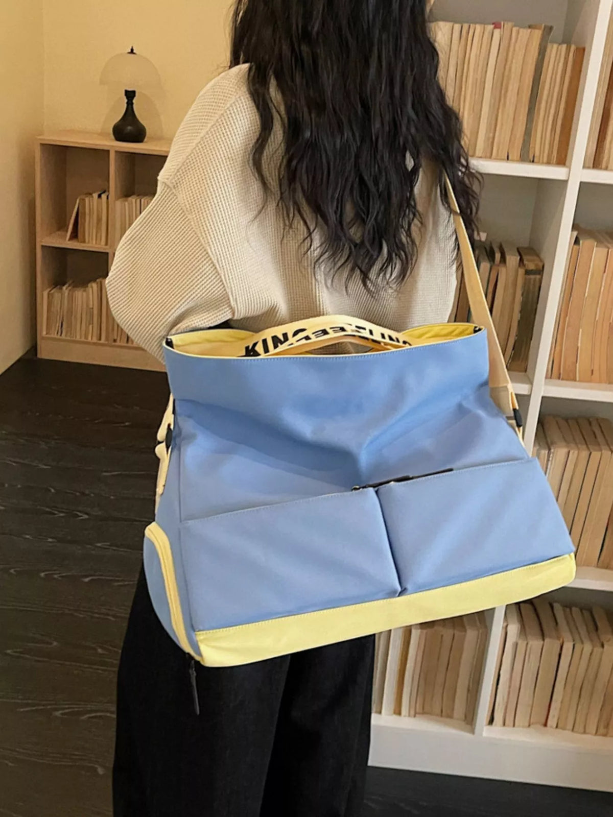 Person holding a blue and yellow bag in a room with bookshelves.