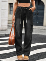 Person wearing black cargo pants with a brown leather handbag on a city street.