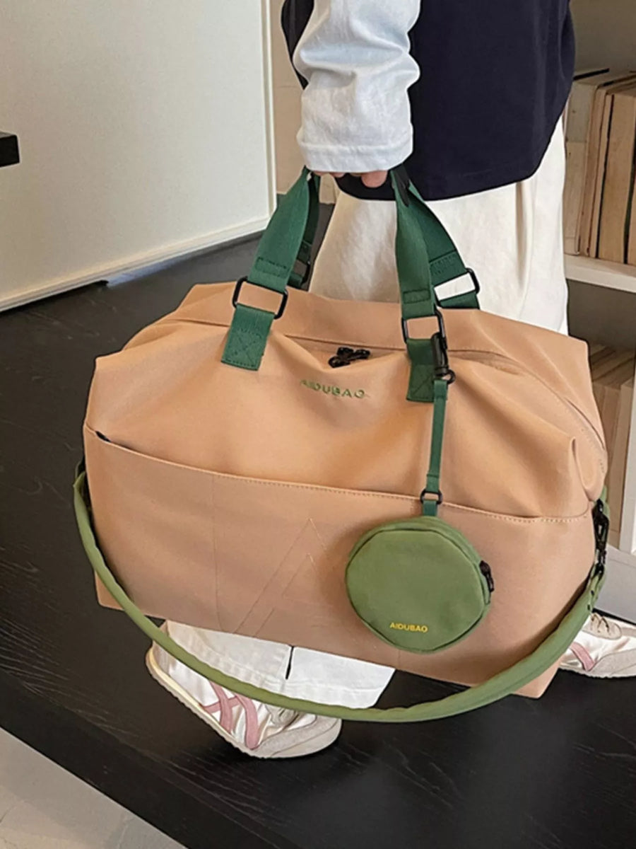Beige duffel bag with green straps and circular pouch held by a person.