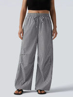 A person wearing loose black-and-white gingham wide-leg pants with an elastic drawstring waist, shown from the chest down against a light gray studio background.