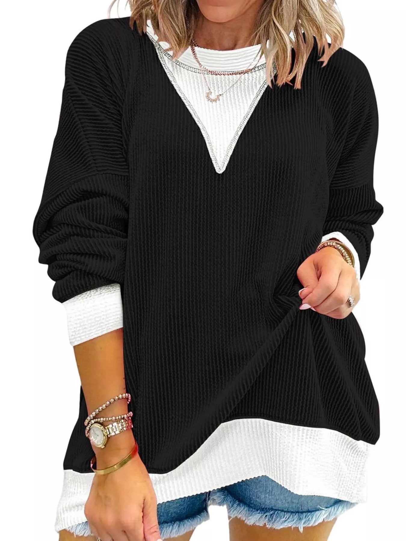 Black sweater with white trim worn by a person on a plain background