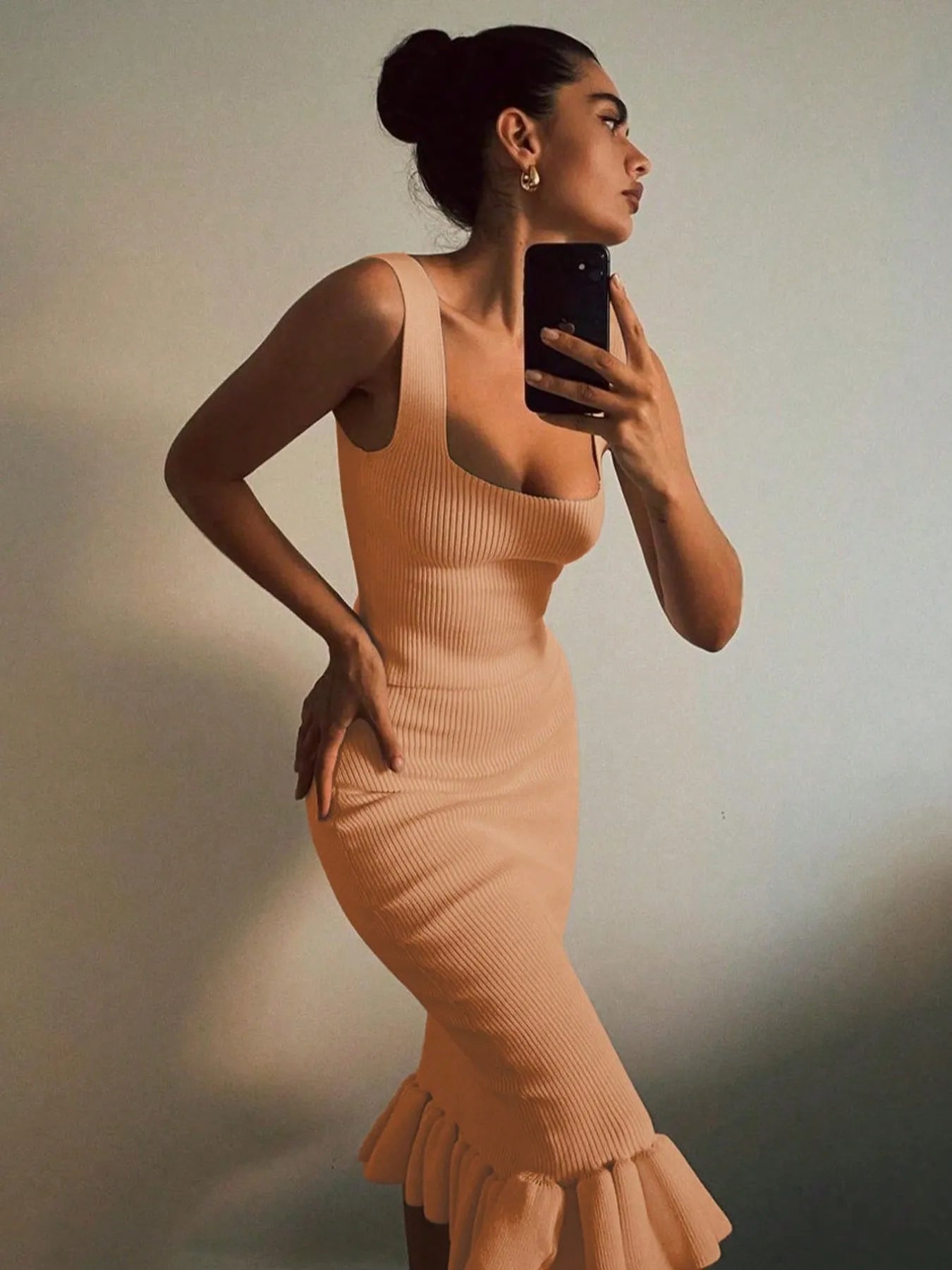 Woman in a beige ribbed dress taking a mirror selfie against a neutral background