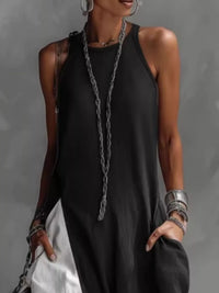 Person wearing a black sleeveless top with a long necklace against a gray background
