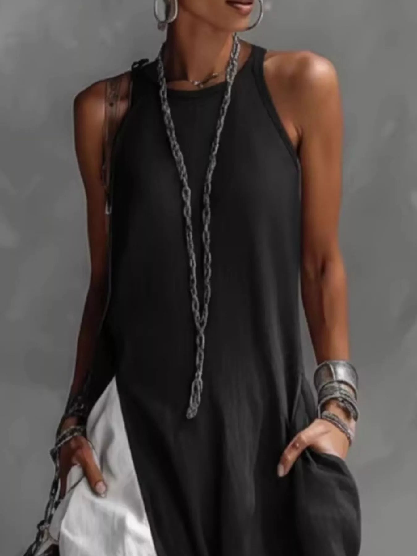 Person wearing a black sleeveless top with a long necklace against a gray background