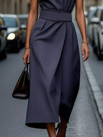 Person wearing a dark blue dress holding a black handbag on a street.