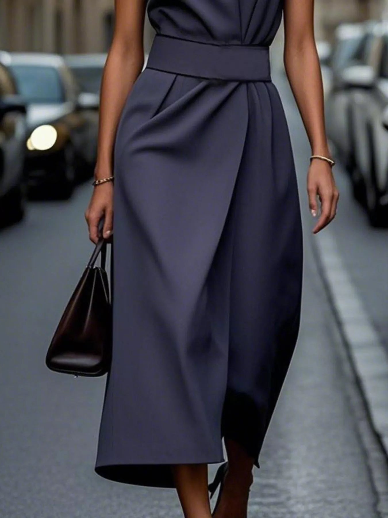 Person wearing a dark blue dress holding a black handbag on a street.