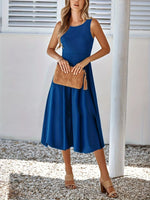 Woman wearing a blue dress holding a brown clutch against a white background