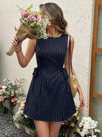Woman in a navy pinstripe dress holding flowers against a textured wall.