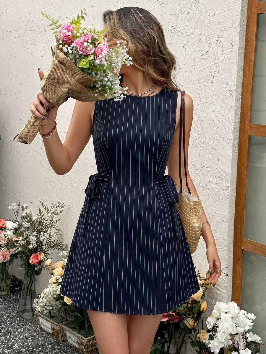 Woman in a navy pinstripe dress holding flowers against a textured wall.