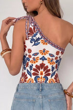 Woman wearing a colorful floral one-shoulder top with denim pants on a white background