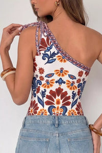 Woman wearing a colorful floral one-shoulder top with denim pants on a white background