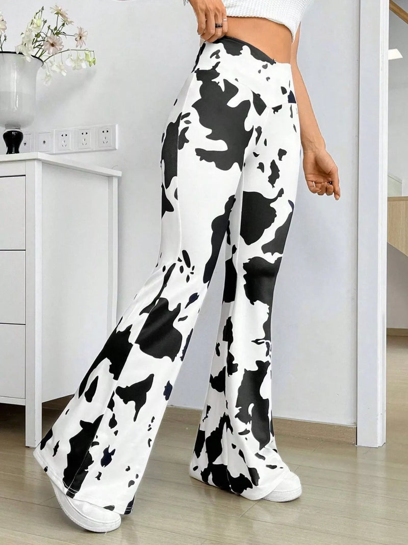 A person wearing high-waisted, wide-leg pants with a black and white cow print pattern, paired with white sneakers in an indoor room setting.