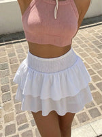 Person wearing a pink crop top and white skirt on a stone pavement.