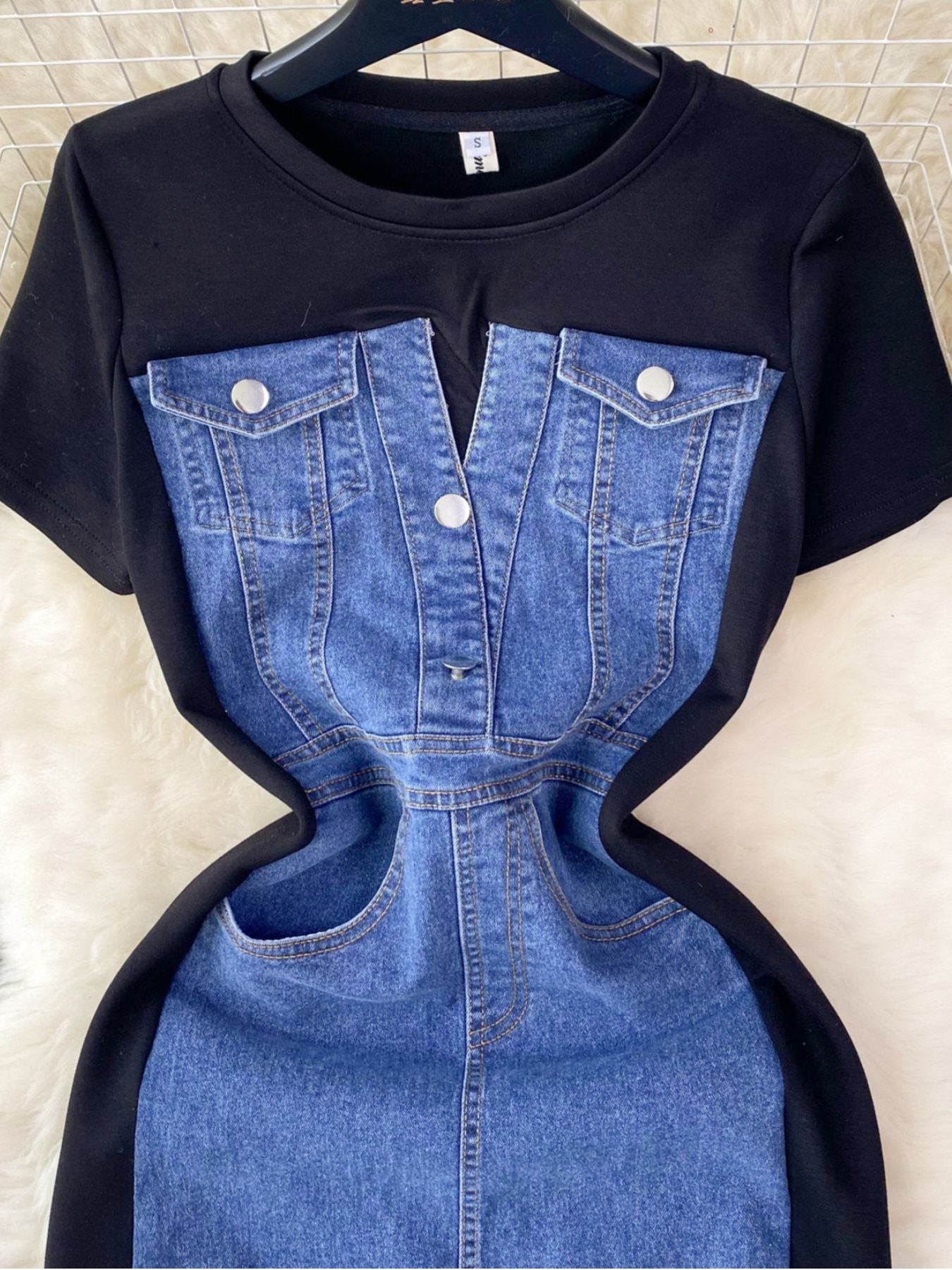 Black t-shirt with blue denim design on a hanger against a tiled wall background