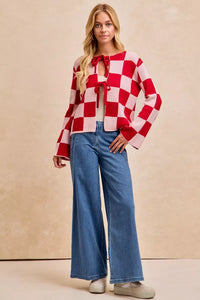 Woman wearing a red and white checkered blouse with a bow and blue jeans against a beige background