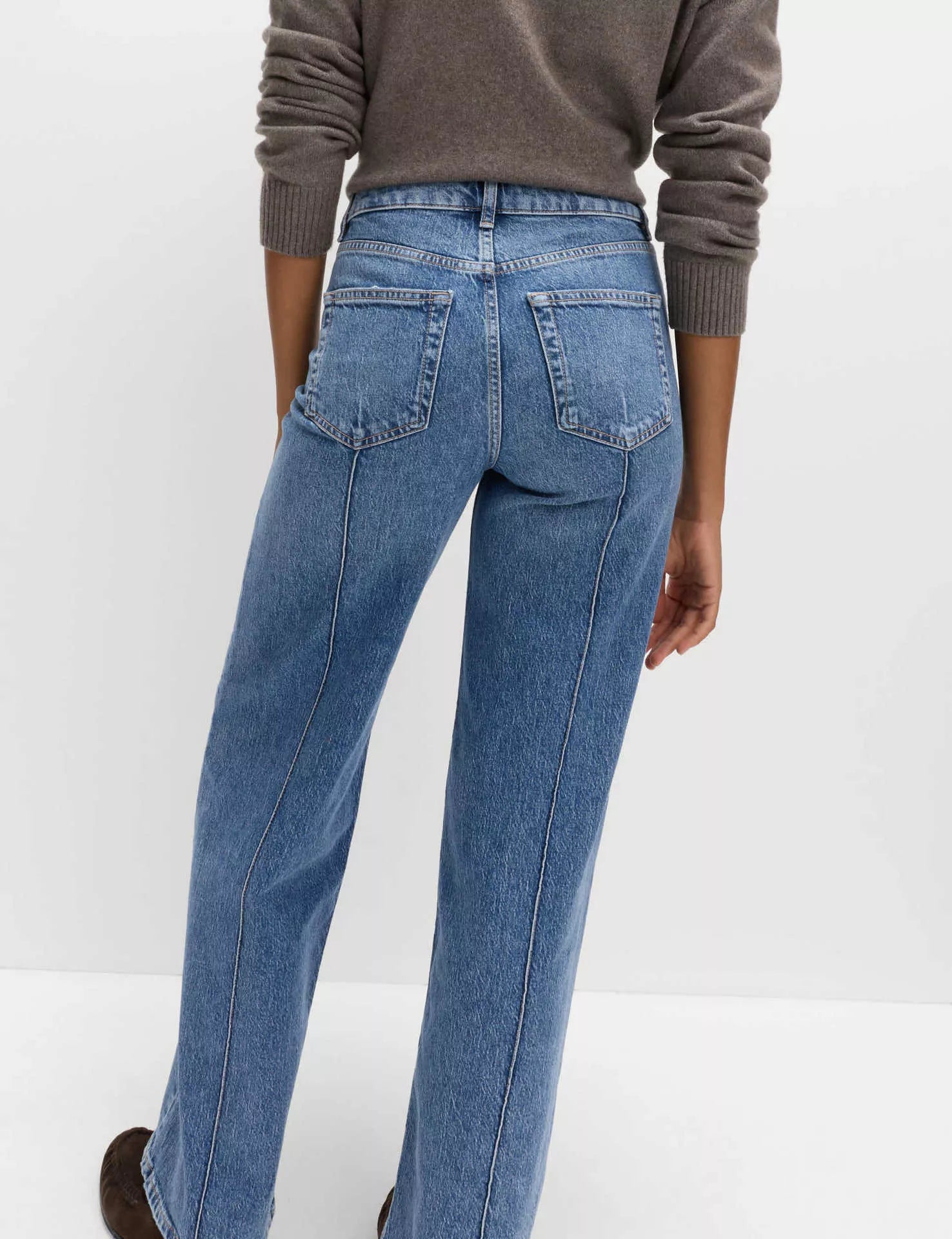 Person wearing blue jeans and a brown sweater on a white background