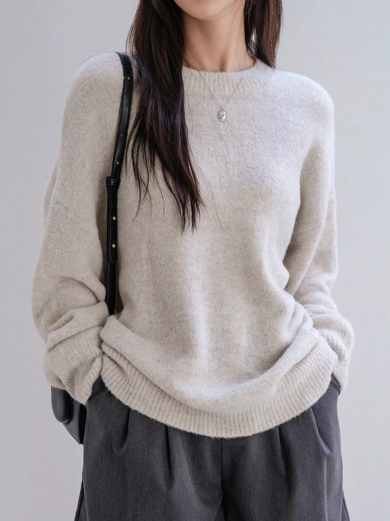 Person wearing a beige sweater and gray pants against a plain background