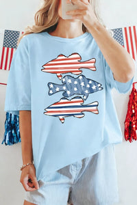 Person wearing a light blue t-shirt with fish designs in American flag colors, standing in front of an American flag.