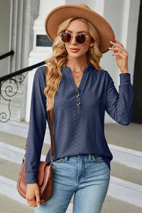 Woman wearing a blue long-sleeve top, beige hat, and sunglasses, standing on a staircase.