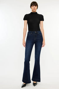 Person wearing a black turtleneck and dark blue flared jeans on a white background