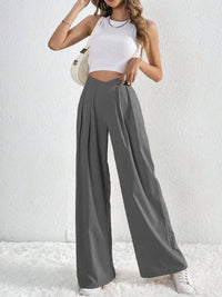 Woman wearing a white crop top and gray wide-leg pants against a white background