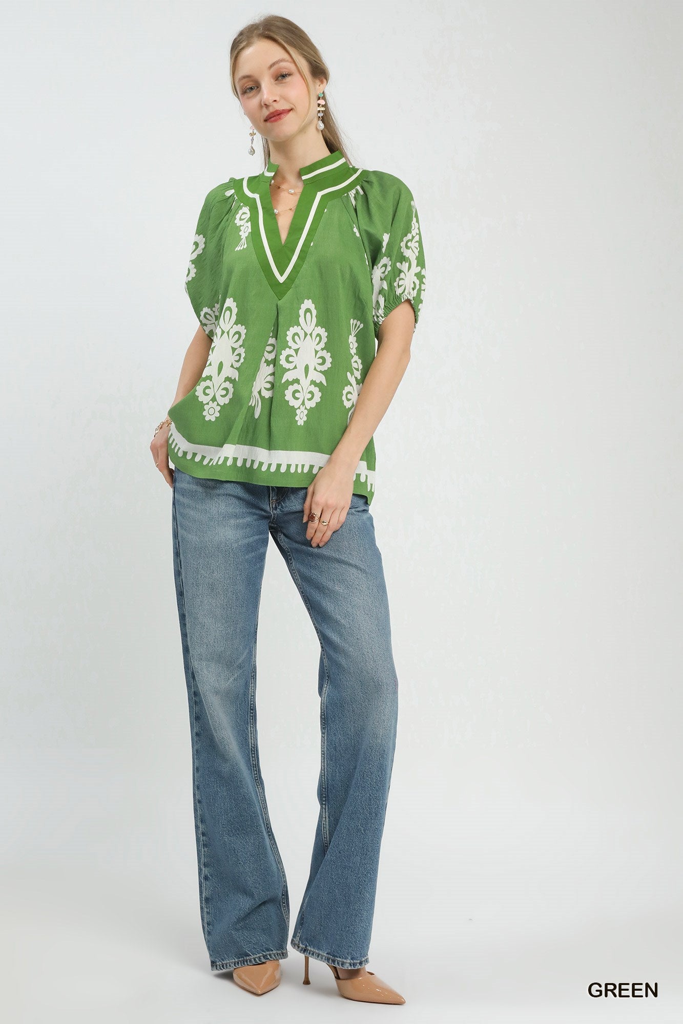 Woman wearing a green patterned blouse and blue jeans on a white background
