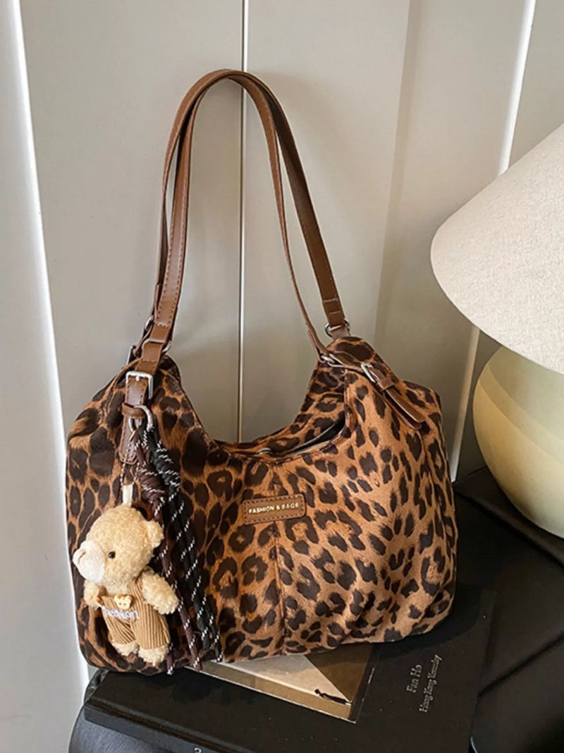 Leopard print handbag with a teddy bear on a dark surface against a white wall.