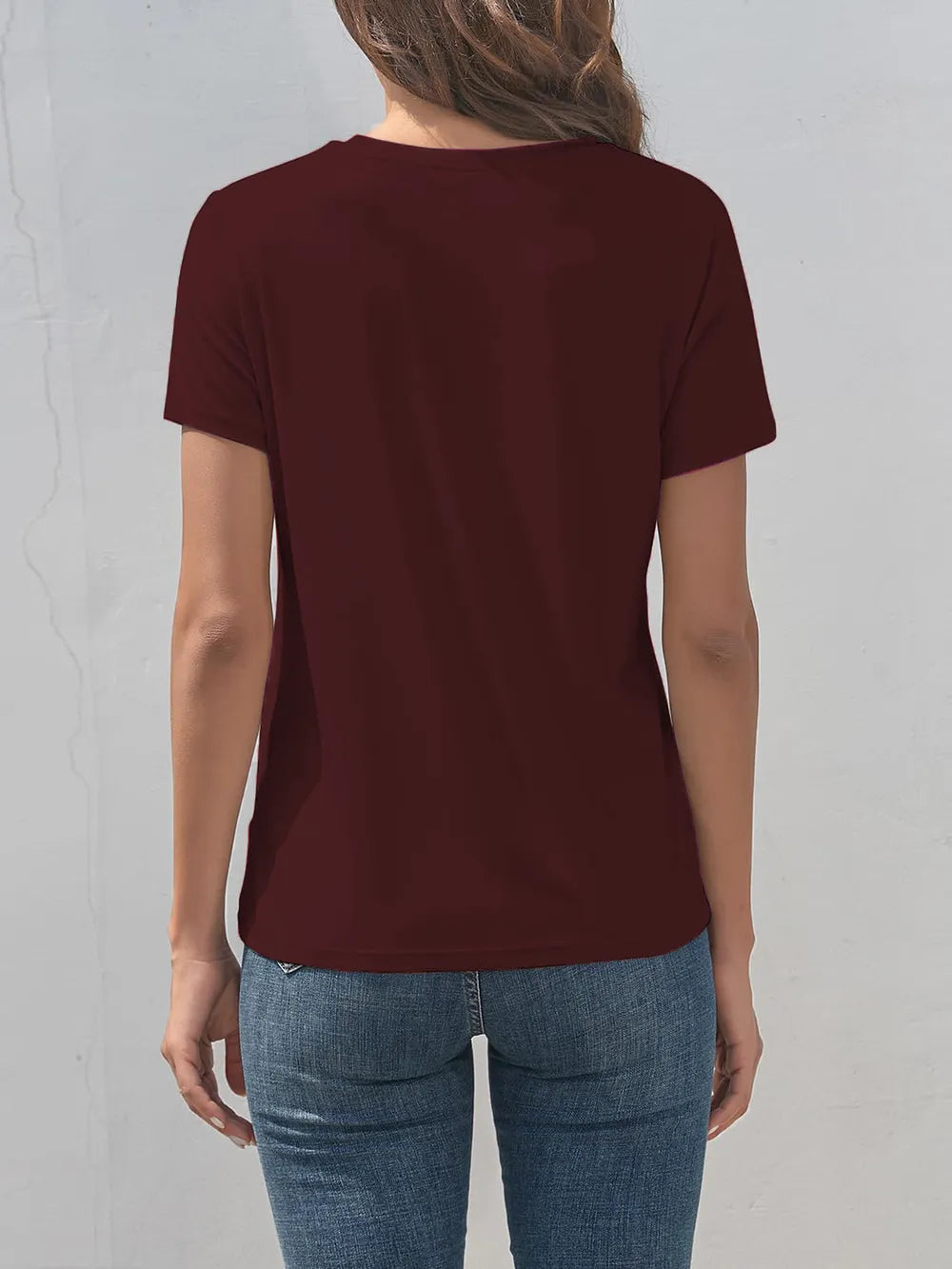 Person wearing a maroon t-shirt and blue jeans against a light gray background