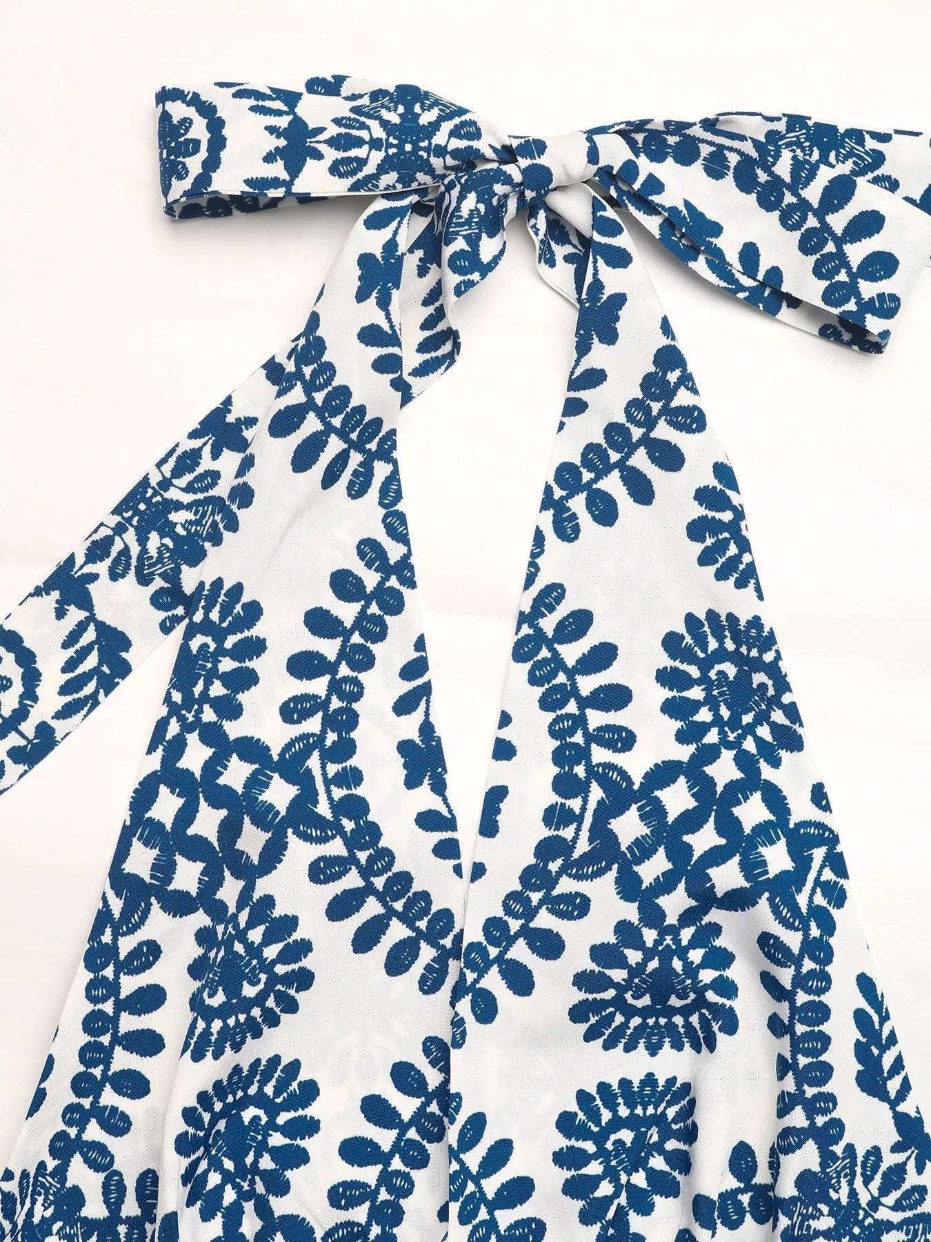 White garment with blue floral pattern and bow detail on a white background