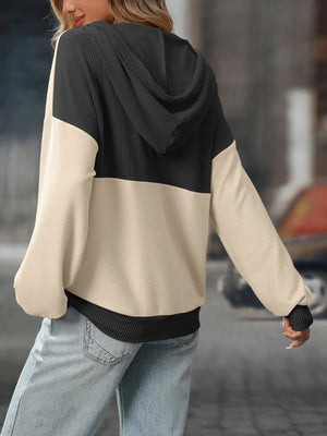 Person wearing a black and beige color-blocked hoodie with blurred background