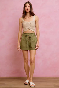 Woman wearing a beige top and green shorts against a pink background