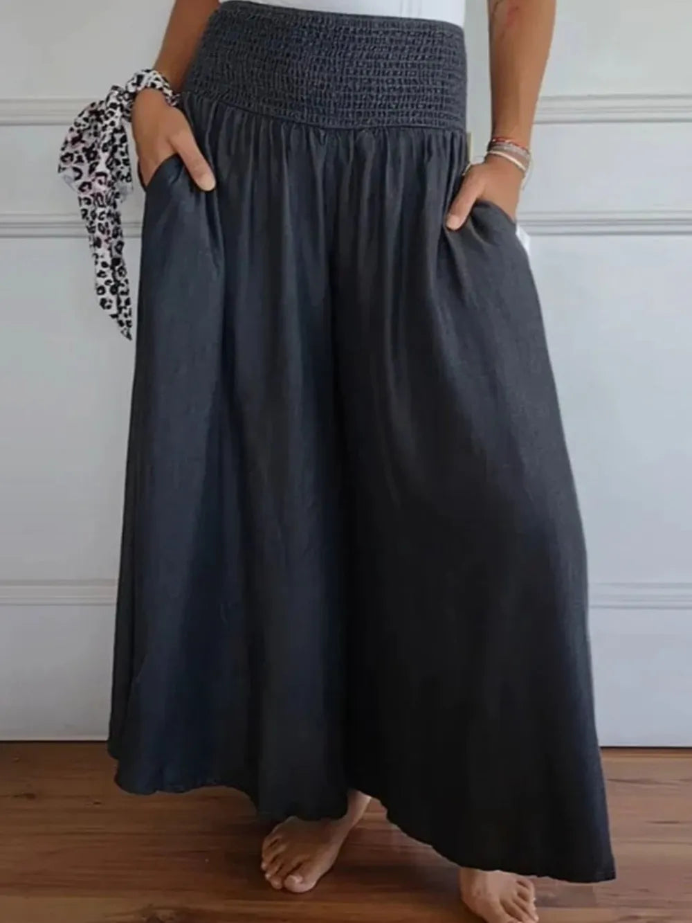 Person wearing a dark gray skirt with hands in pockets against a white wall.