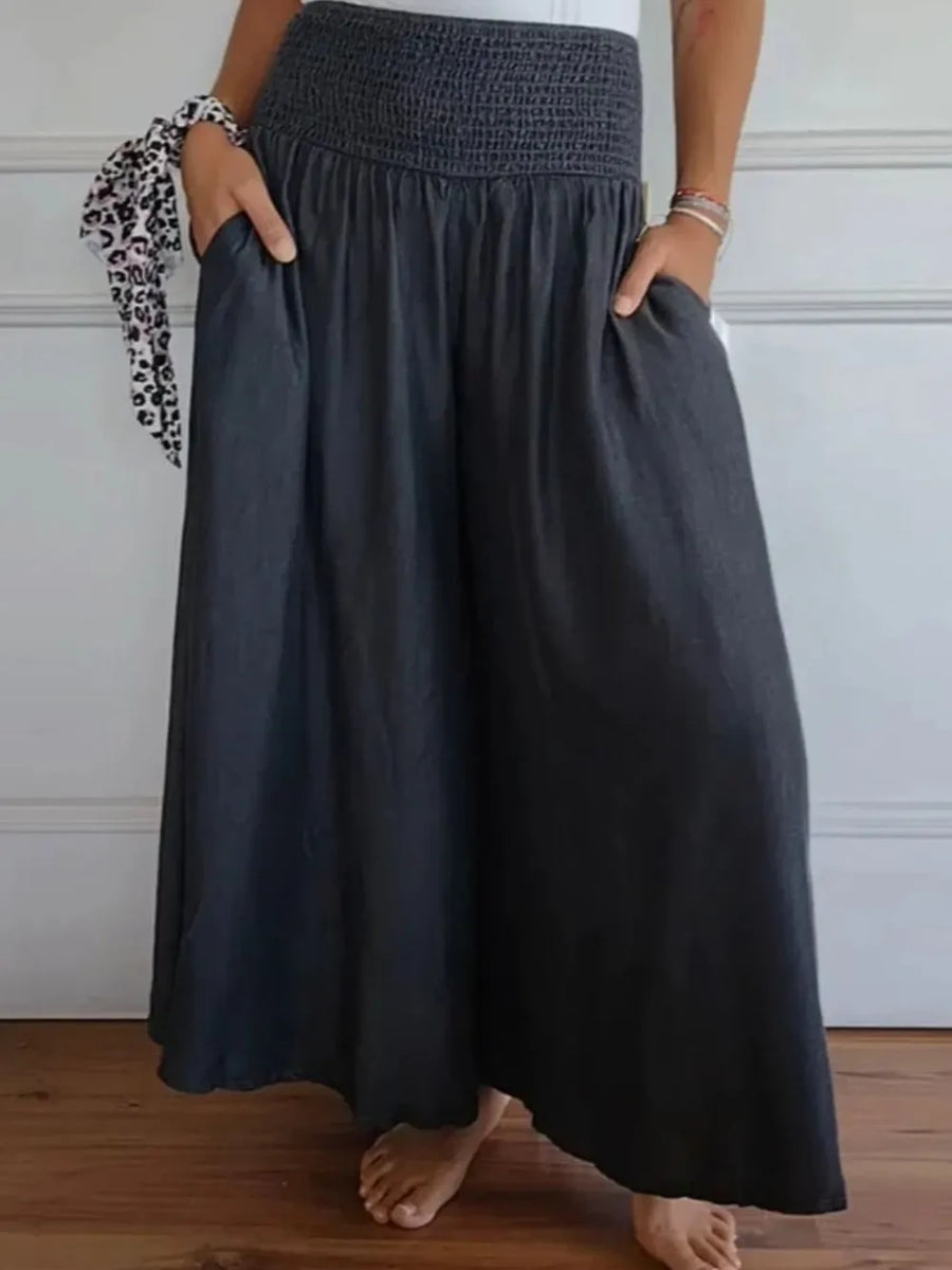 Person wearing a dark gray skirt with hands in pockets against a white wall.