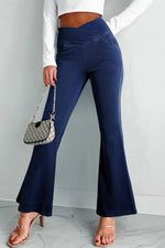 Person wearing navy flared pants with a white top and small handbag on a light gray background
