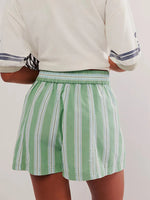Person wearing a white shirt with blue stripes and green striped shorts on a plain background