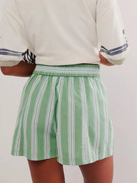 Person wearing a white shirt with blue stripes and green striped shorts on a plain background