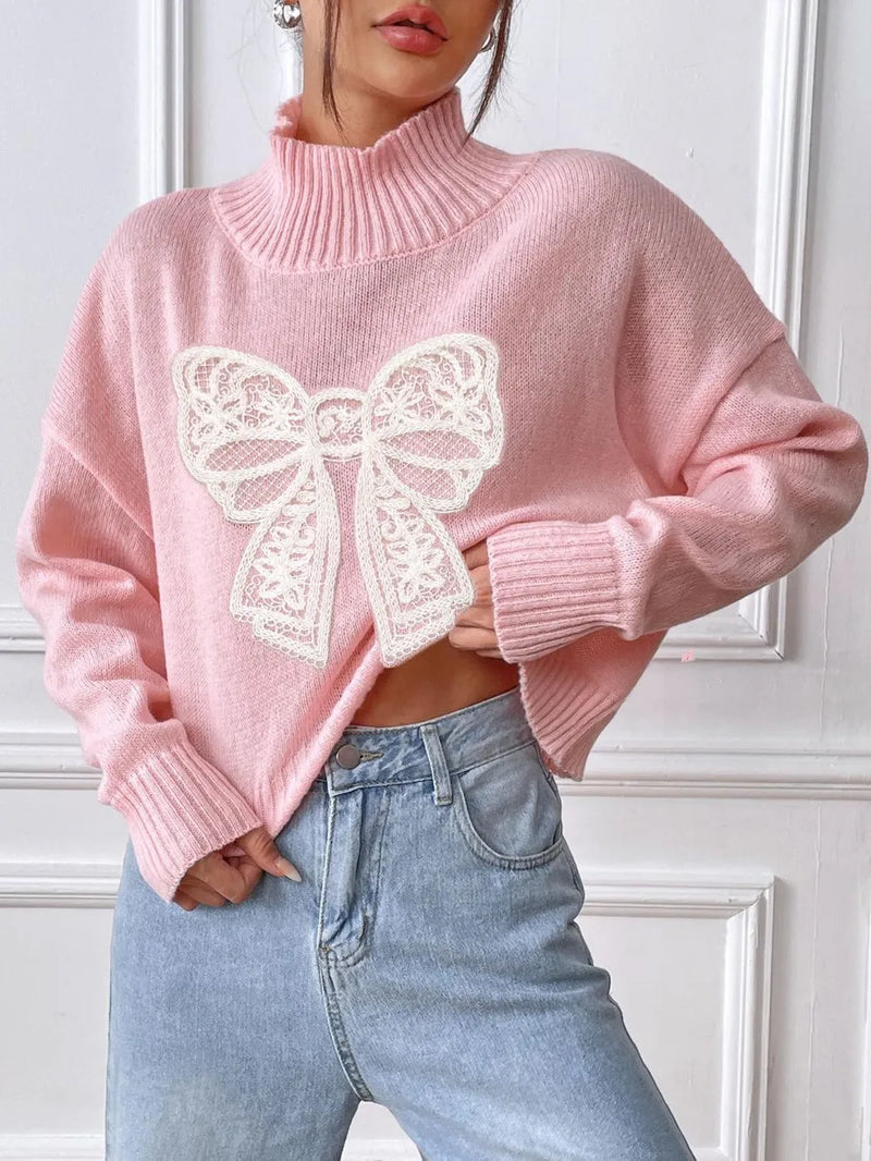 Person wearing a pink sweater with a white lace bow design and blue jeans.