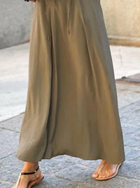 Long beige skirt worn by a person on a stone pavement.