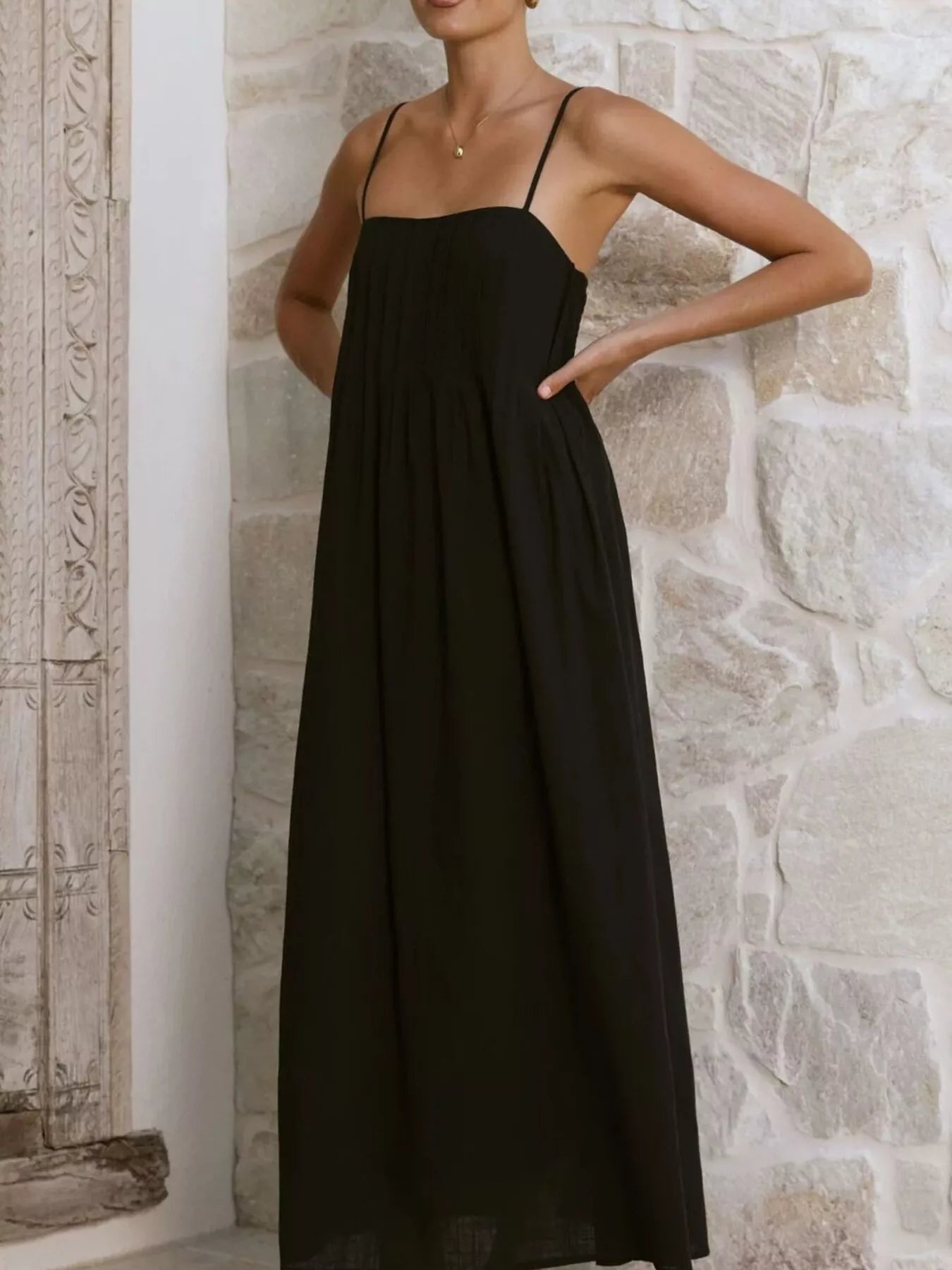 Woman wearing a black dress against a stone wall.