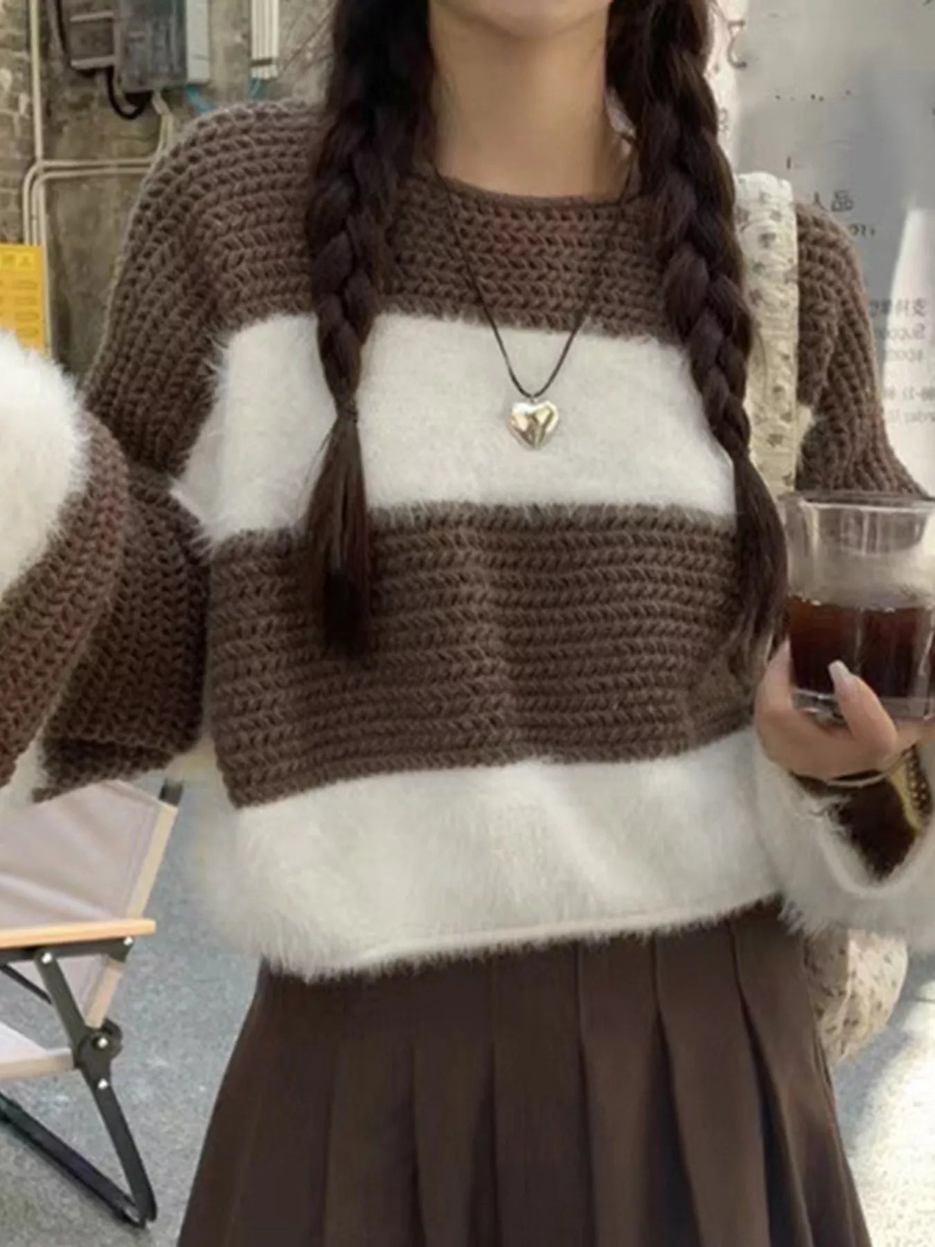 Person wearing a brown and white sweater holding a drink.
