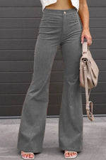 Person wearing gray flared pants holding a beige handbag against a gray wall.