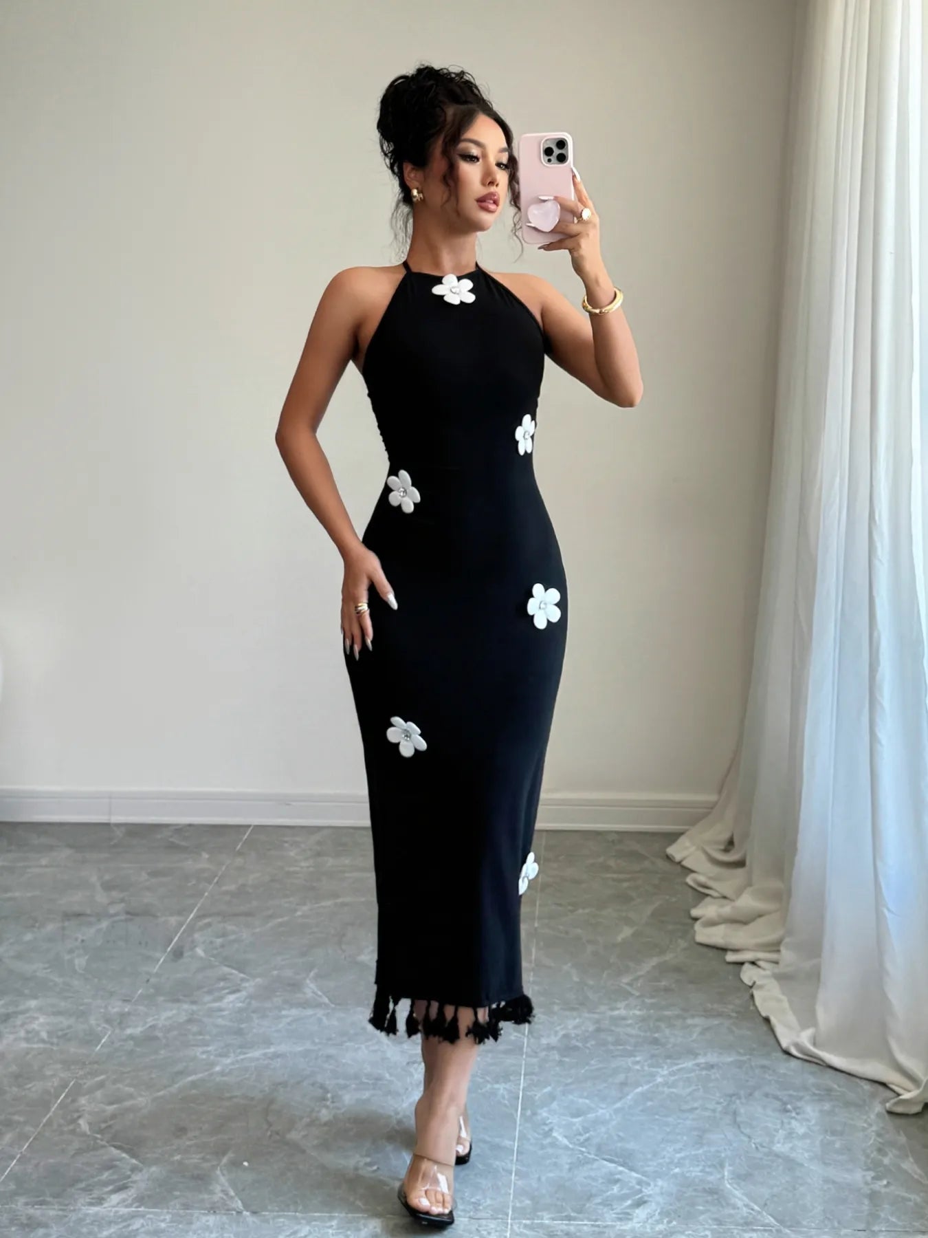 Woman wearing a black dress with white floral patterns taking a mirror selfie.