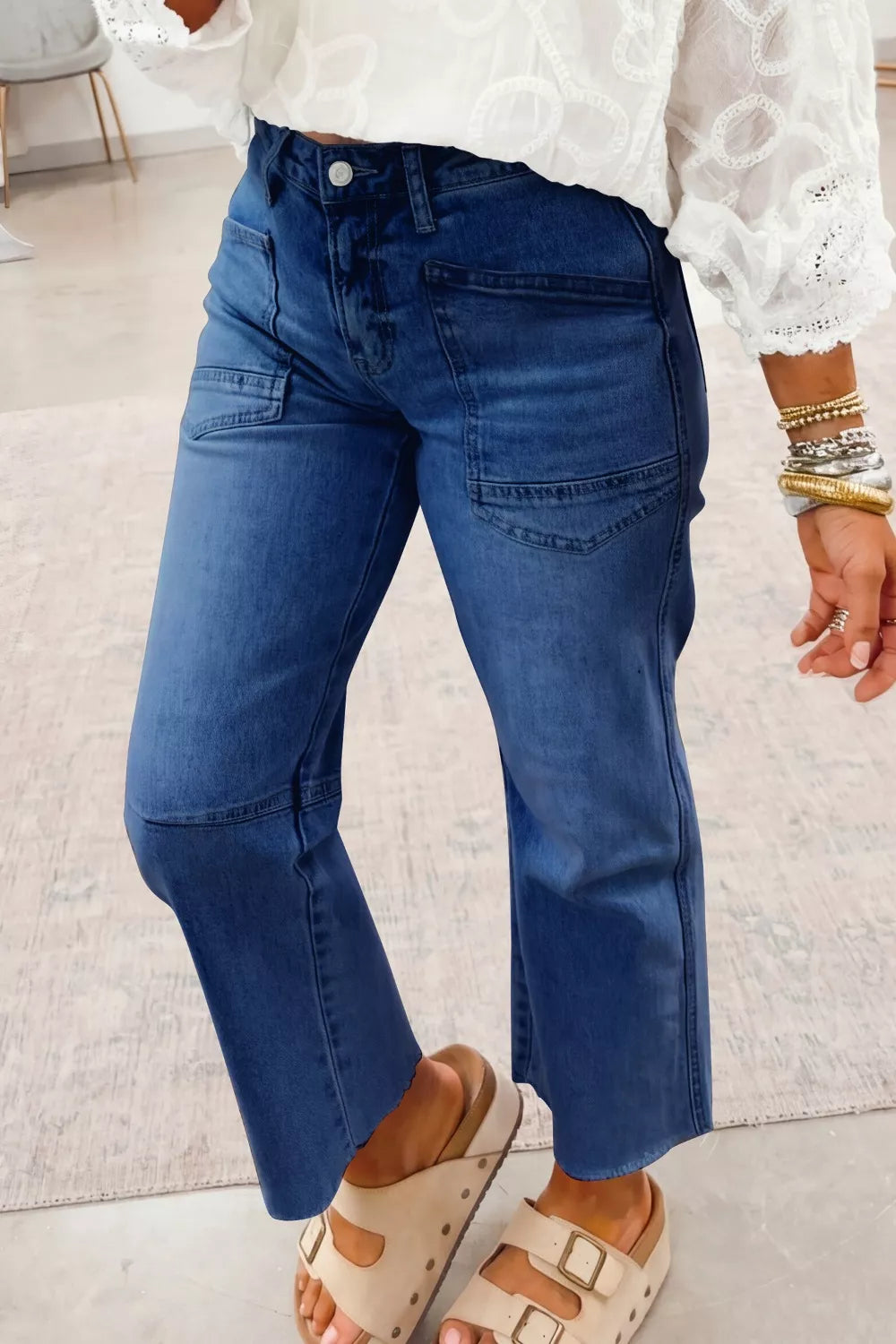 Person wearing blue jeans and white lace top on a light background