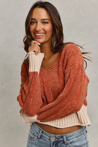 Woman wearing a rust-colored sweater over a beige top with a gray background