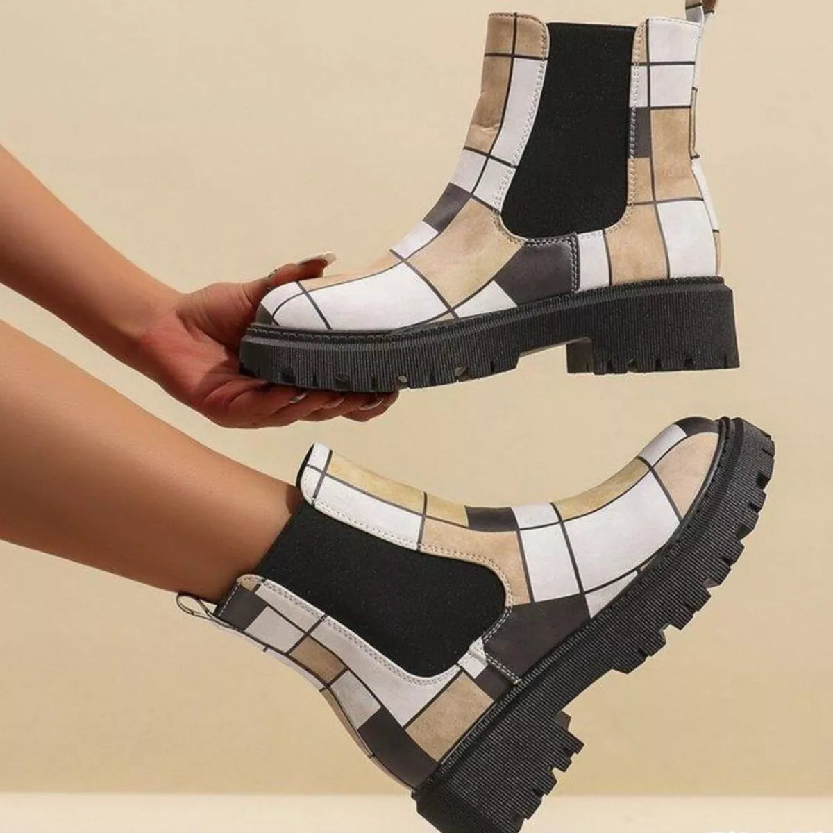 Patterned boots being held above a beige background