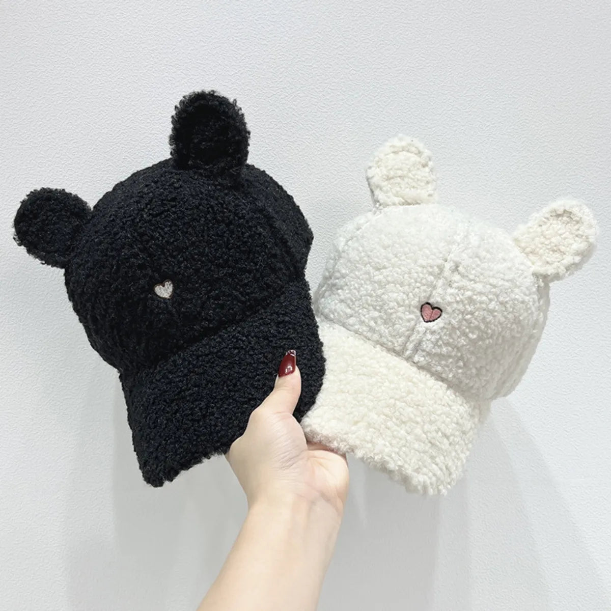 Black and white beanies with heart details held by a hand against a light gray background