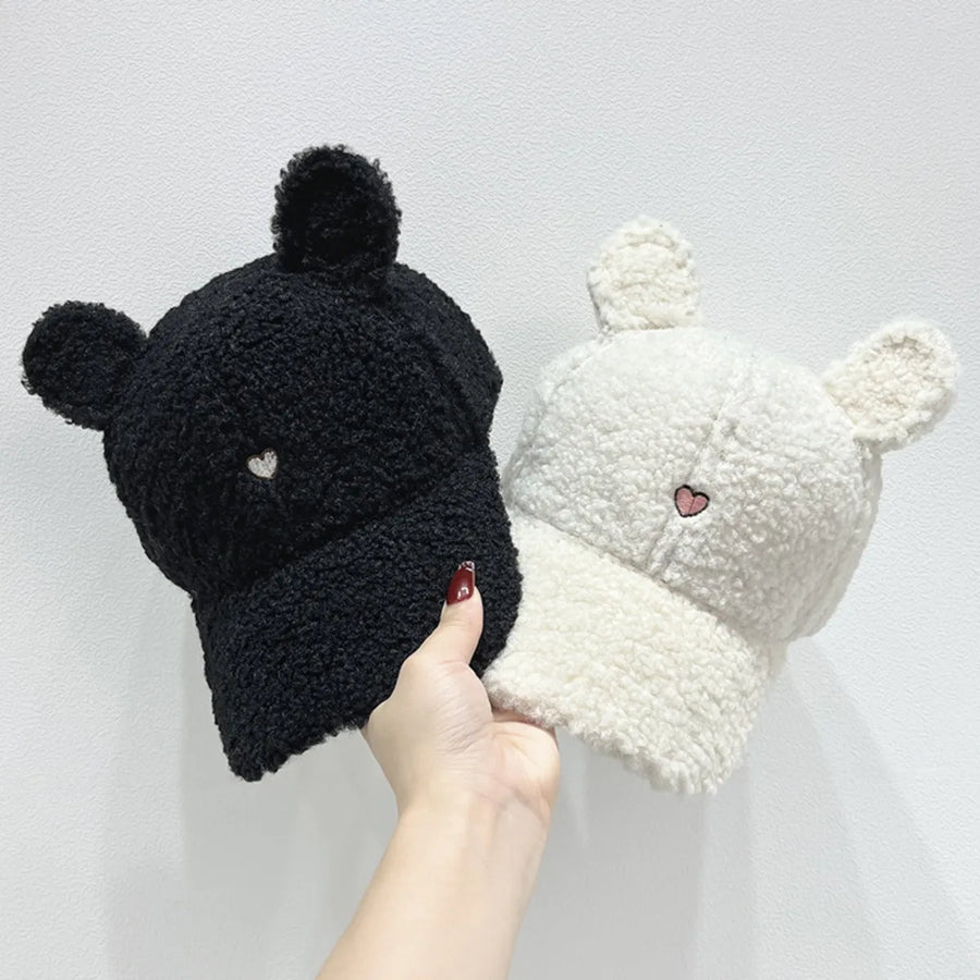 Black and white beanies with heart details held by a hand against a light gray background