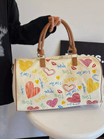 Handbag with colorful heart designs and text held by a person.