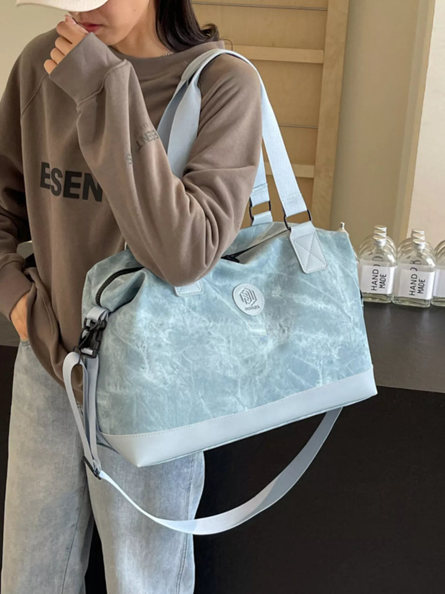 Person holding a light blue tote bag with a visible brand logo, wearing a brown sweatshirt.